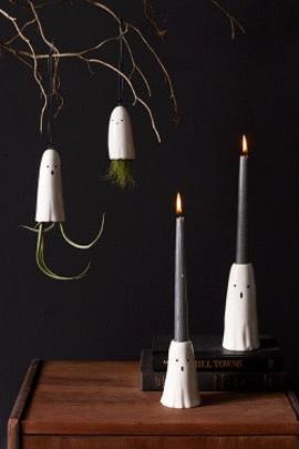 Ghost candleholders with black tapers in dark eerie setting.