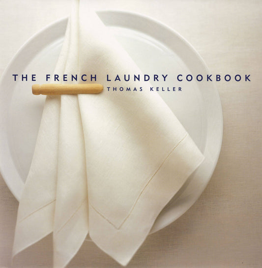 Close-up of The French Laundry Cookbook cover with a folded linen napkin on a white plate