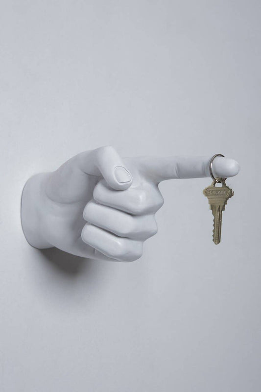 Tall view of the white pointing hand wall hook holding a brass house key on a ring