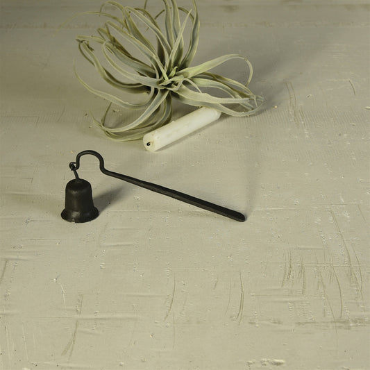 black hand-forged iron snuffer on concrete with candle and air plant in background