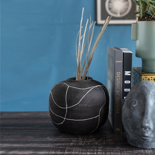 Black vase with white abstract stripes next to books