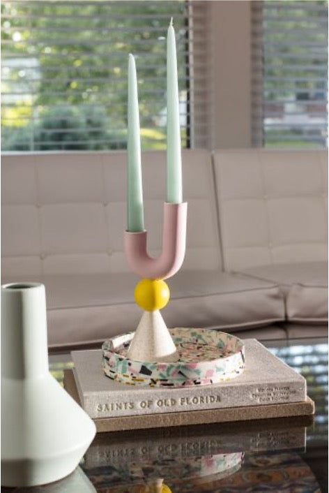 Geometric candle holder in white, yellow, and pink colors with marine taper candles on stack of books.