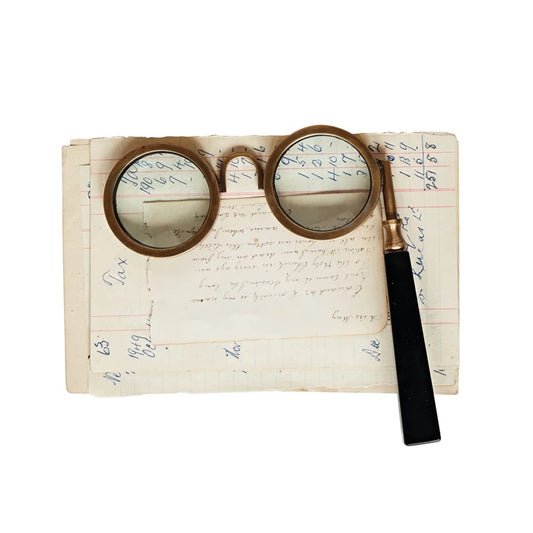 Brass spectacle magnifying glass with black handle on vintage paper
