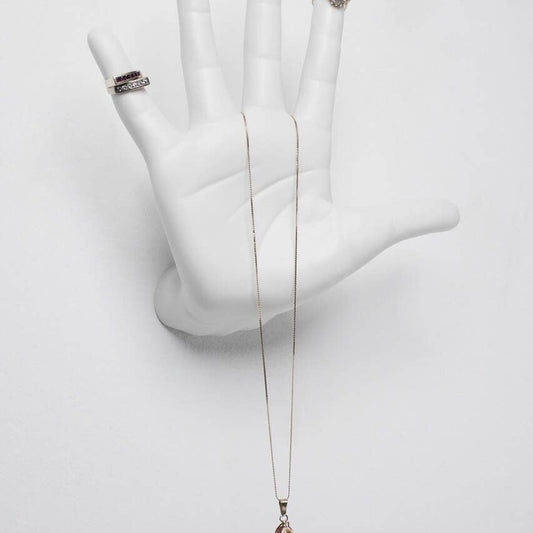 White ceramic talk to the hand wall mount close up, holding stacked rings and a long gold necklace