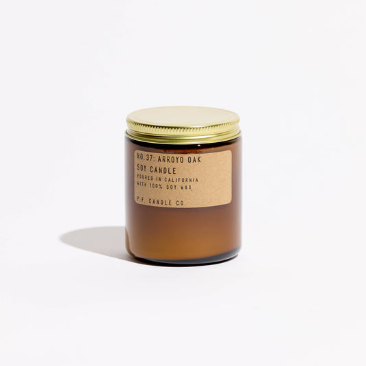 Amber glass jar soy candle with brass lid and kraft label reading No. 37 Arroyo Oak