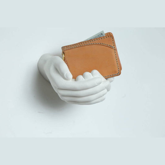White criss-cross hands wall sculpture cradling a tan leather wallet with cash, square view
