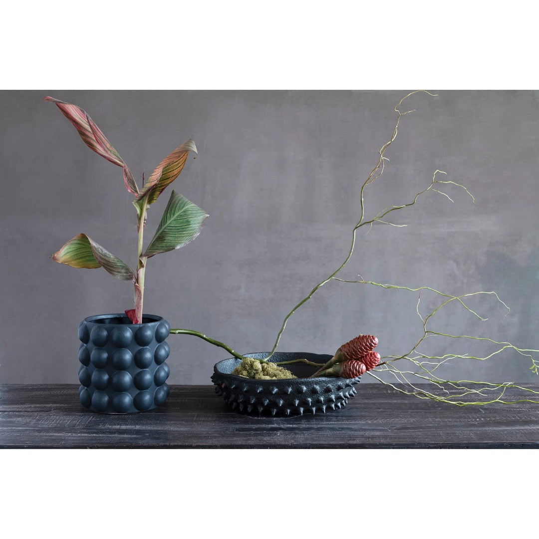 Black spike terracotta bowl filled with moss and dried floral next to modern vase. 