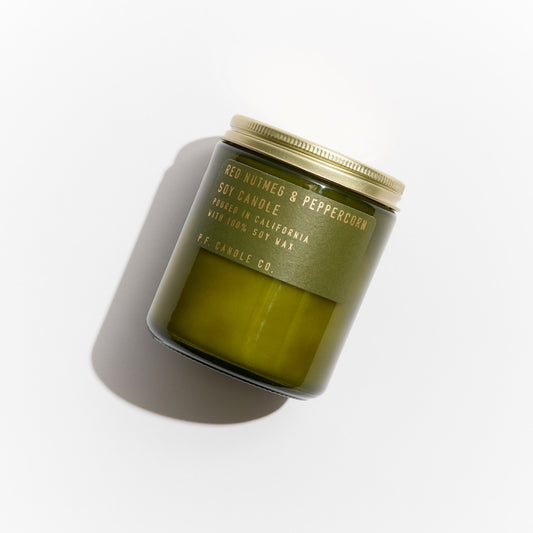 Red Nutmeg & Peppercorn candle in green glass jar with gold embossed green label and brass lid. 