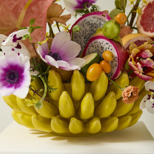 Yellow ceramic banana bowl filled with fruit and flowers