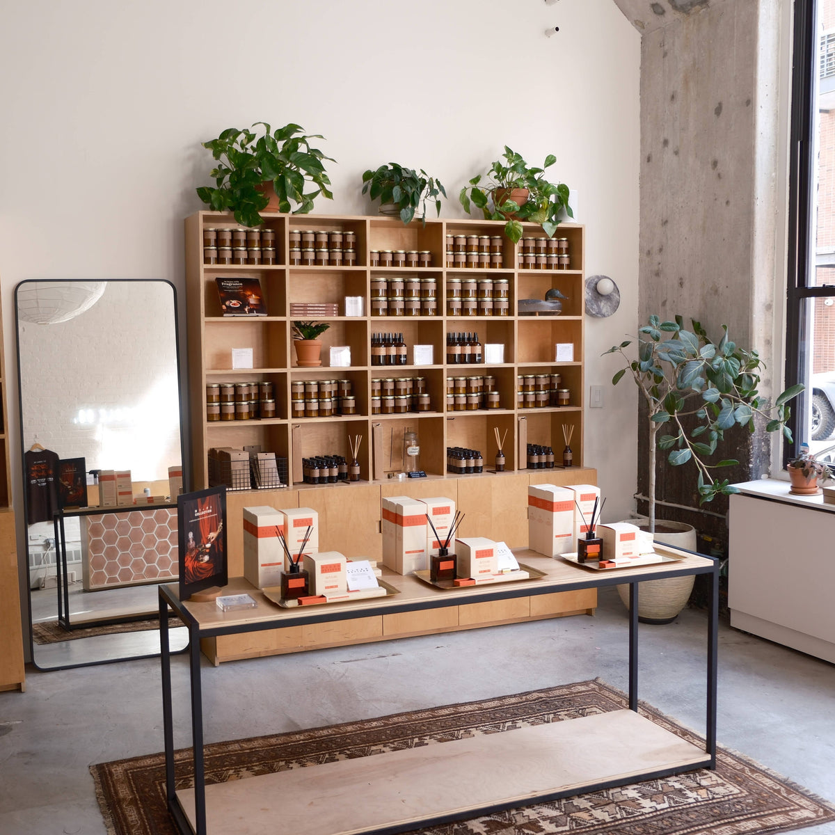 Candle shop interior with wooden shelves of amber jar candles, plants, and a table of diffusers on a rug