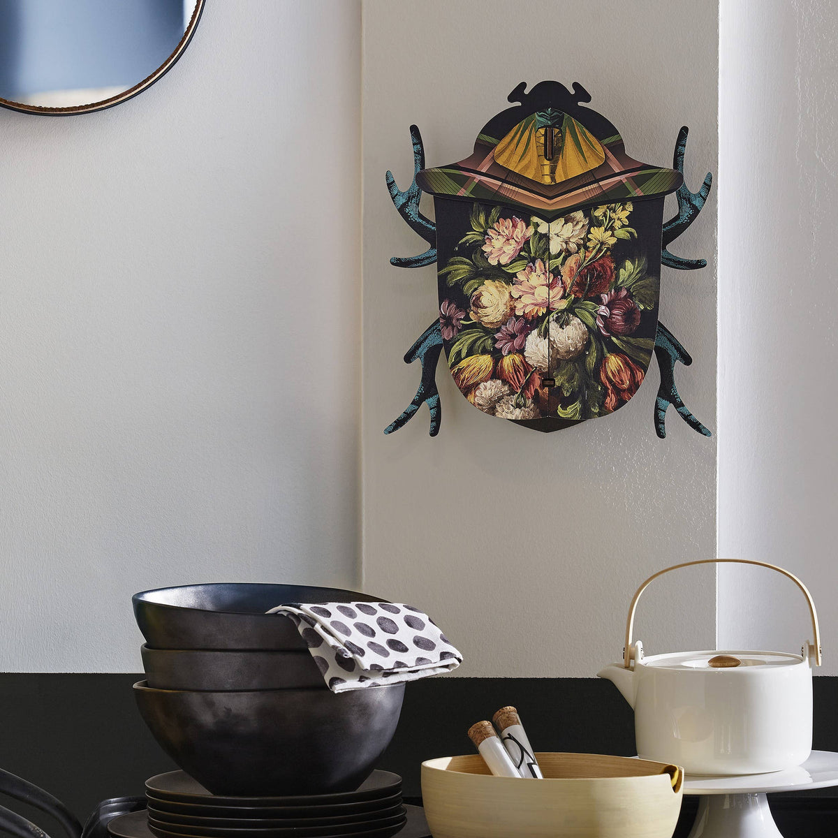 Keith floral beetle box hung on a white kitchen wall above dark stoneware bowls and a white teapot