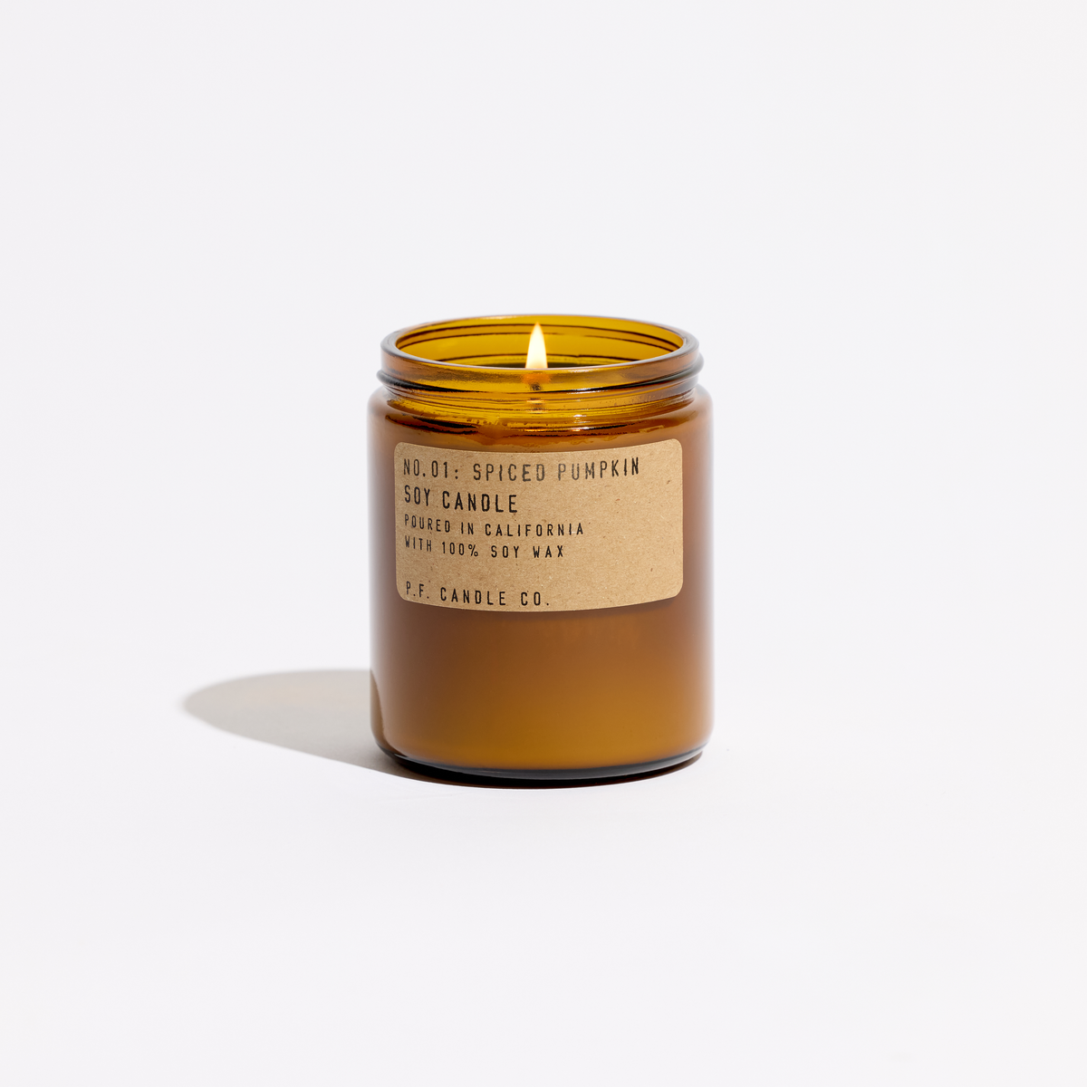 Lit Spiced Pumpkin soy candle in an amber jar without its lid, flame visible