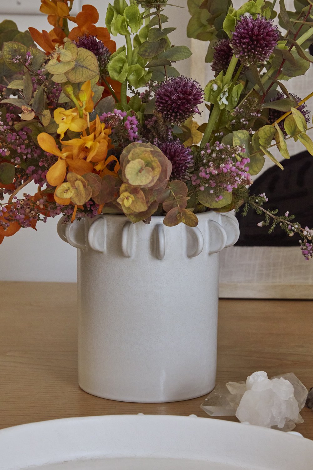 Reverie canister filled with allium, orchids, eucalyptus and dried stems on a wood table