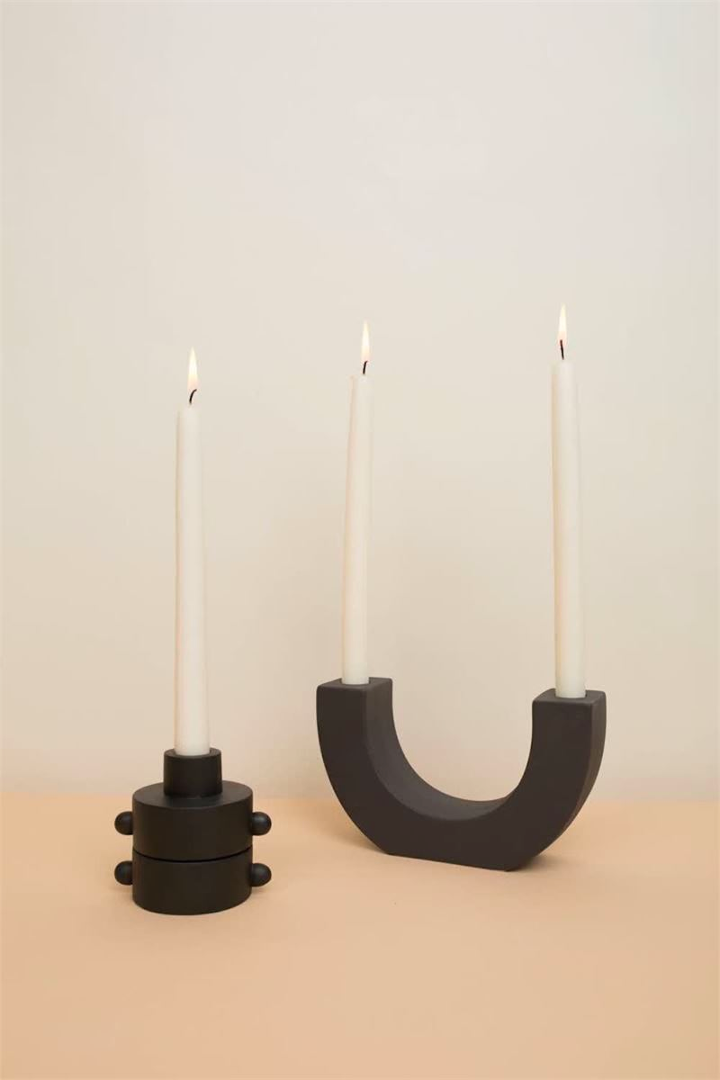 black u-shape ceramic double taper holder with 2 lit candles next to 2 black round single taper holder with lit candle