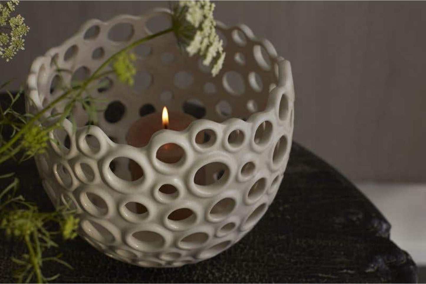Ceramic pot with holes and a lit candle inside