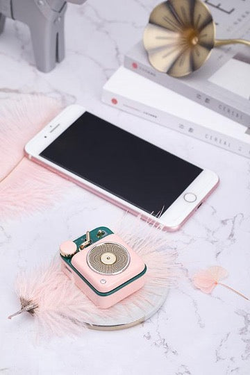 Cotton candy button speaker on pink feather and white marble top next to white iphone