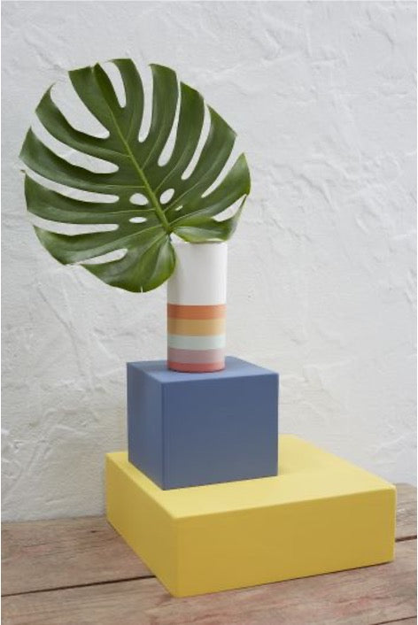 Cylinder vase with monstera leaf on top of colored cubes. 