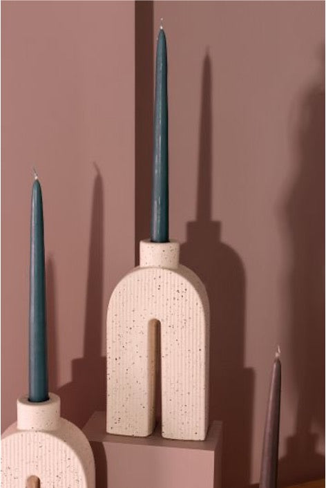 Collection of 3 u-shape sculptural single taper candle holders in 3 sizes with a matte white and black speckle finish; with assorted tapers. Mauve background.
