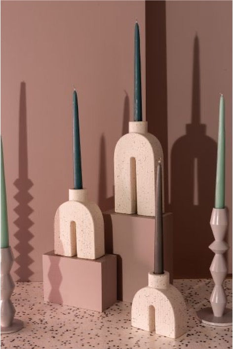 Collection of 3 u-shape sculptural single taper candle holders in 3 sizes with a matte white and black speckle finish; with assorted tapers. Mauve background.