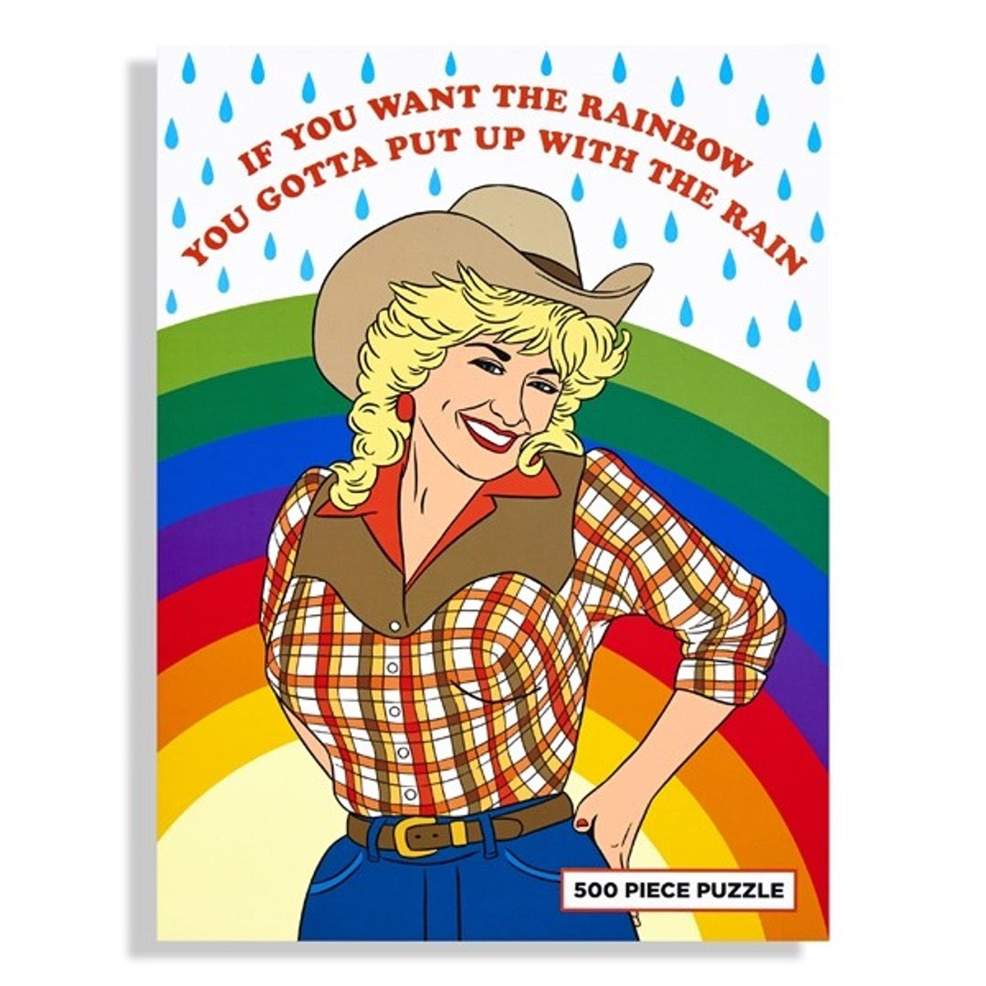 Dolly Parton puzzle in cowgirl outfit with rainbow and raindrops in background and text above in red that reads "If you want the rainbow, you gotta put up with the rain" Front of box