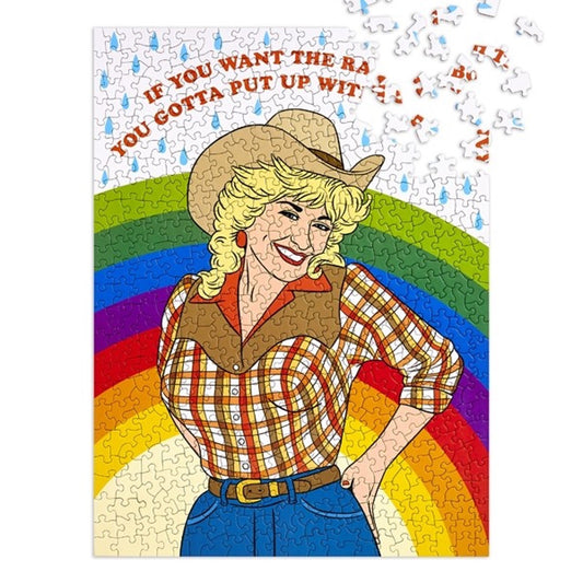 Dolly Parton puzzle in cowgirl outfit with rainbow and raindrops in background and text above in red that reads "If you want the rainbow, you gotta put up with the rain"