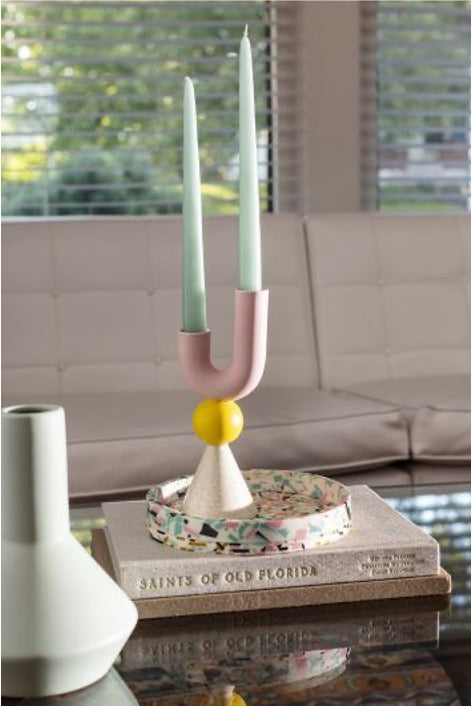 Geometric candle holder in white, yellow, and pink colors with marine taper candles on stack of books. 