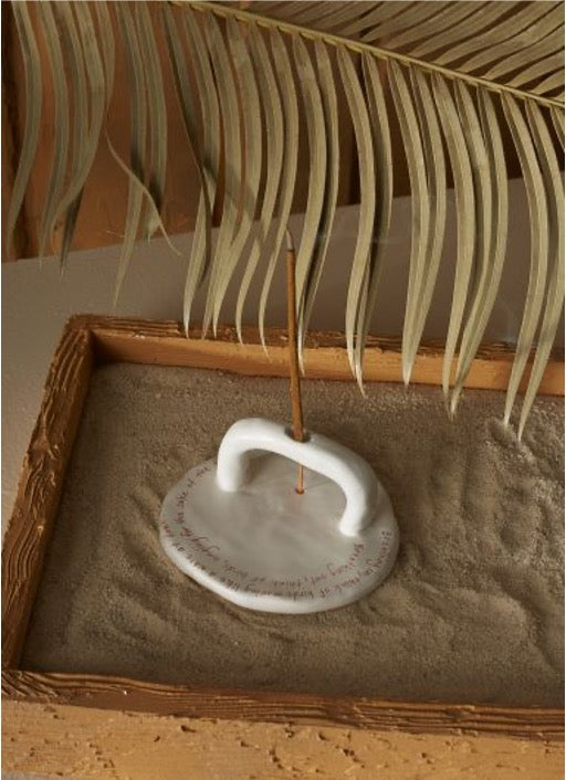 Round incense holder in white with an upright semi-arched holder with incense stick on a tray filled with sand.