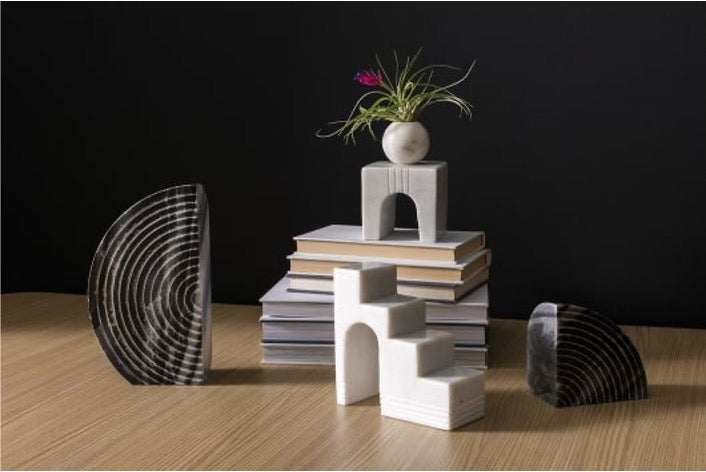 White marble geometric sculptures on a stack of books with black spherical bookends.