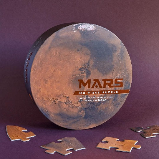 Mars puzzle in round box with full image of planet Mars with puzzle pieces on burgundy background.