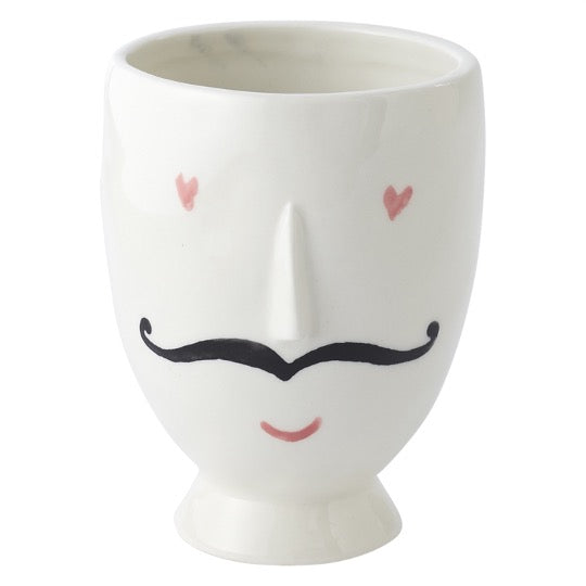 Footed white pot with pink heart eyes, black mustache, pink lips and raise nose.