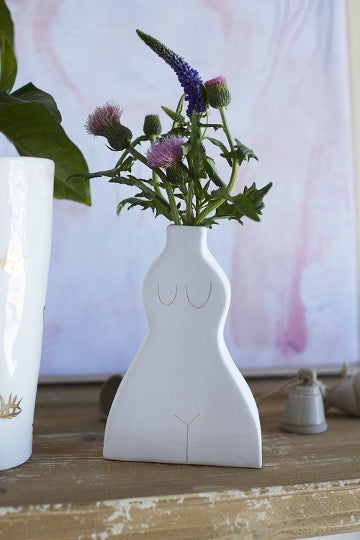 White ceramic budvase in female silhouette with flowers on distressed wood table