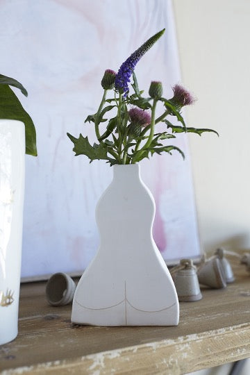 White ceramic budvase in female silhouette with flowers on distressed wood table