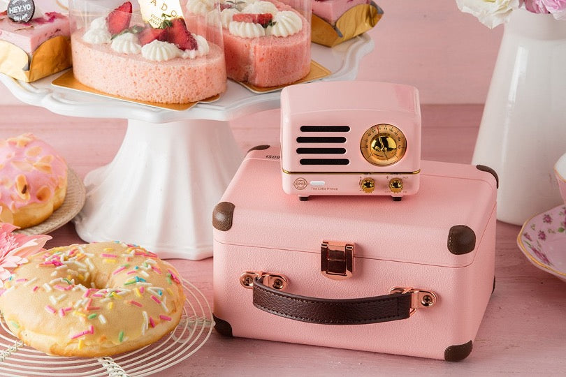 Pink OTR metal speaker on pink box surrounded by pastries. 