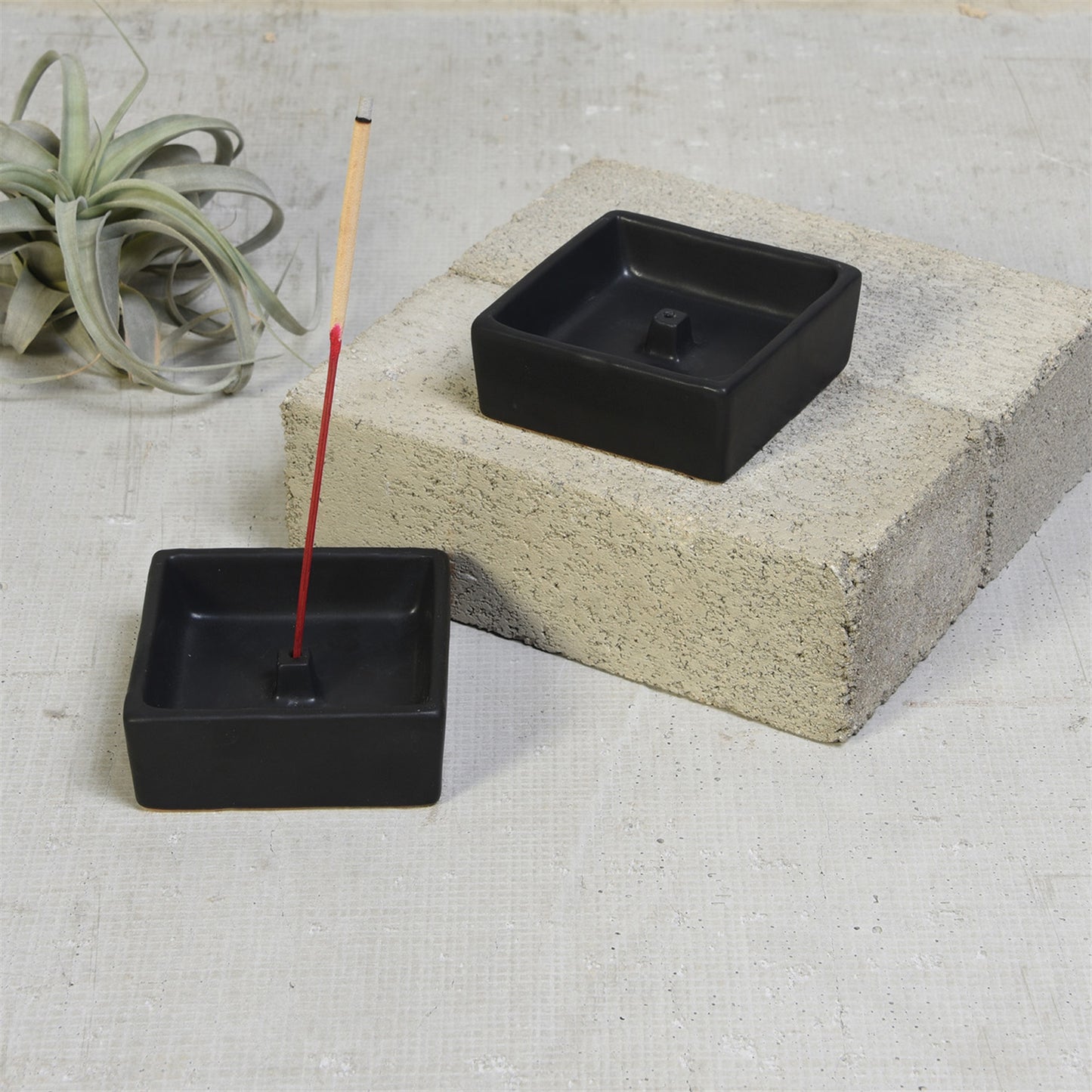 pair of mate black incense holder with incense stick on concrete with air plant in background