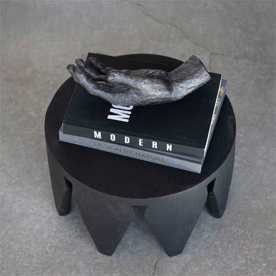 resin hand sculpture in black on top of books on black side table.