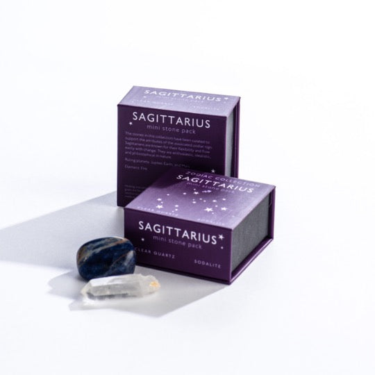 Sagittarius mini stone pack text on purple boxes with Sagittarius constellation pattern. Clear quartz and polished sodalite stones in front. 