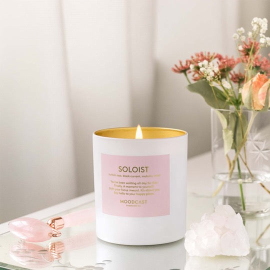 Soloist Candle, lit on table with pink flowers.