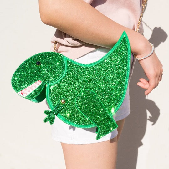 Woman holding T-Rex novelty handbag in green with glitter side with gold finish chain strap.