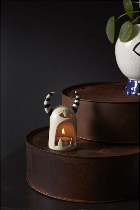 Monster tealight holder with one eye and black and white striped horns. With lit tealight on round rusted tin table