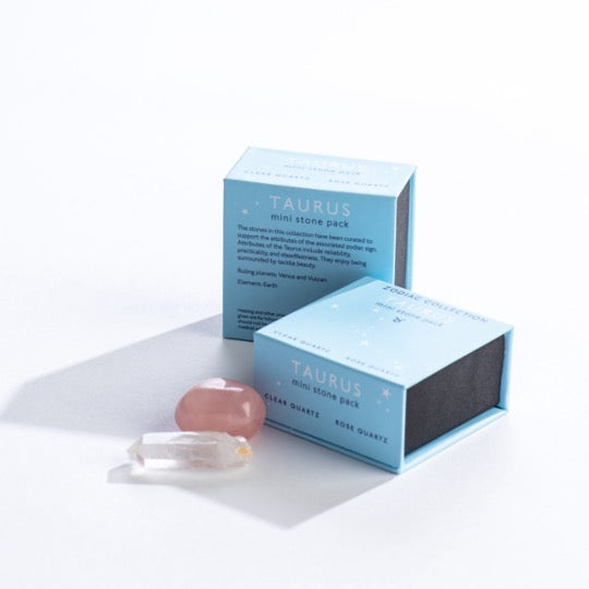 Taurus mini stone pack text on light blue boxes with Taurus constellation pattern. Clear quartz and polished rose quartz stones in front. 