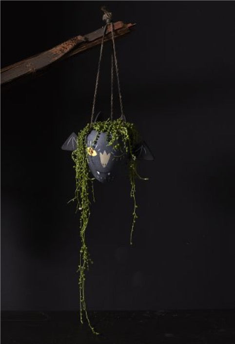 Concrete hanging pot with vampire face and wings, suspended on twig with hanging flowers
